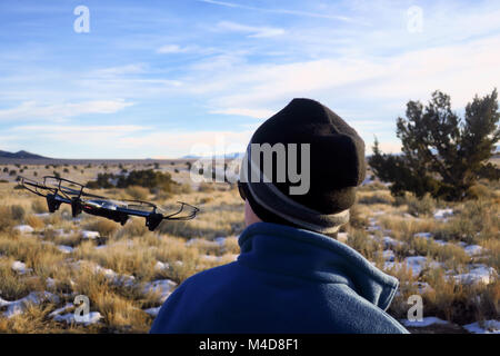 A boy flying a gray drone banking to the right in the snow patched Utah desert. Stock Photo