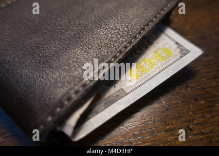 A one hundred dollar bill sticking out of a brown leather bi fold wallet. Stock Photo