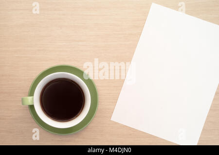 A green cup of coffee on the background of a table and a white sheet of paper simulates the beginning Stock Photo