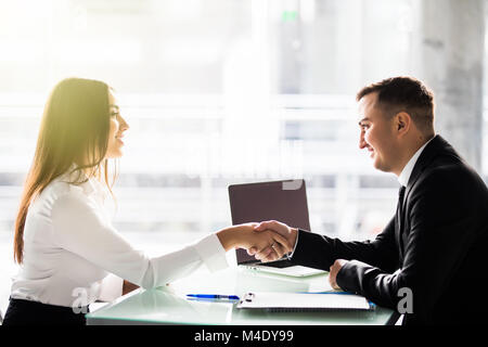 Side view of man and woman partners shaking hands over the table, maintaining eye contact, confident entrepreneurs ready for effective negotiations, e Stock Photo