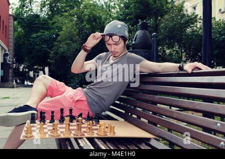 Young adult sitting on a bench and playing chess Stock Photo