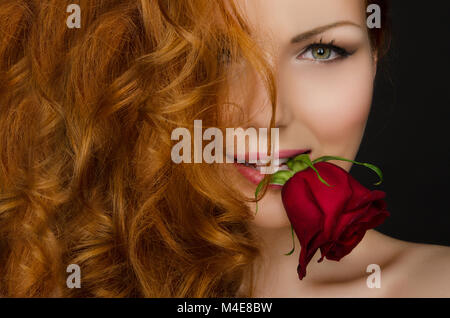 woman with red hair holds rose in her mouth Stock Photo