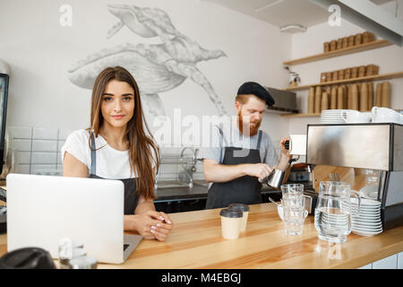 Coffee Business Concept - Positive young bearded man and beautiful attractive lady barista couple enjoy working together at the modern coffee shop Stock Photo