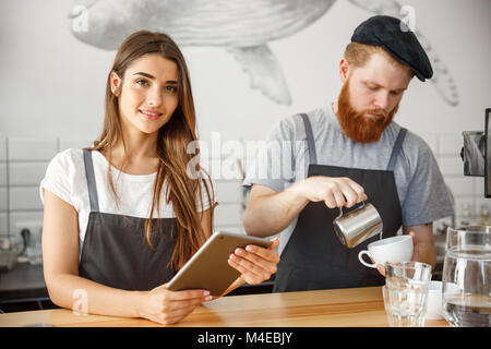 Coffee Business Concept - Cheerful baristas looking at their tablets for online orders in modern coffee shop. Stock Photo