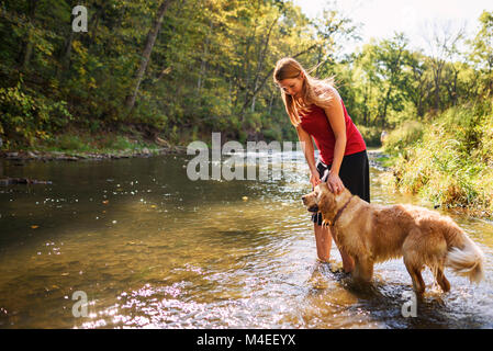 Woman standing in a river with a golden retriever dog Stock Photo