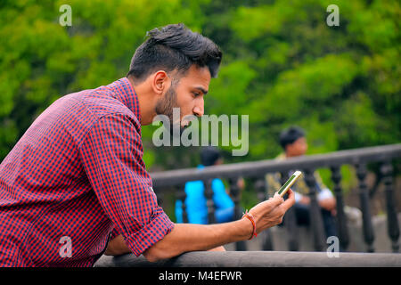 Young man with checked shirt looking at cell phone, Pune, Maharashtra. Stock Photo