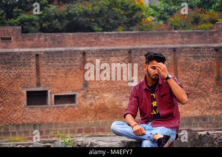 Young man with checked shirt sitting on stones with brick wall background, Pune, Maharashtra. Stock Photo