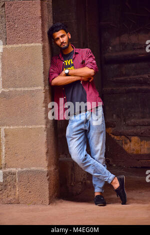 Young man with checked shirt leaning on wall, Pune, Maharashtra. Stock Photo