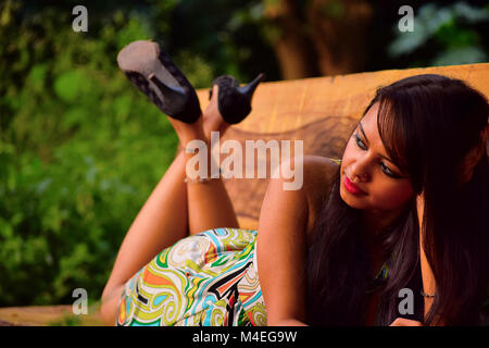 Young girl looking lying on stomach on bench with legs crossed. Pune, Maharashtra. Stock Photo