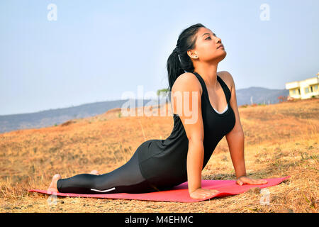 Young Indian girl doing fitness exercise - Bhujangasana or  Cobra Pose. Mountain backdrop, Pune, Maharashtra. Stock Photo