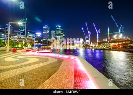 Walkway at Elizabeth Quay marina, Esplanade with modern skyscrapers and construction cranes on the Swan River in Perth Downtown with night lighting, Western Australia. Stock Photo