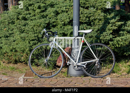 White men's bicycle against a metal pole on a paved road with a knapsack attached to it Stock Photo