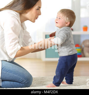 Side view portrait of a mother helping his son to walk on the floor at home