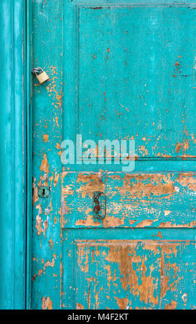 Old turquioise wooden door with peeling paint and rusty lock and handle Stock Photo
