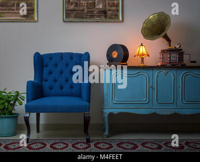 Interior shot of blue armchair, vintage wooden light blue sideboard, lighted antique table lamp, old phonograph (gramophone), vinyl records Stock Photo