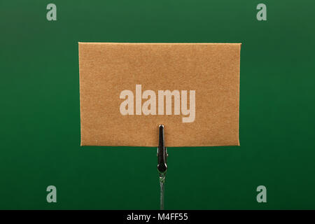 Blank brown kraft cardboard paper parchment sign with copy space on metal note holder over green background, front side view Stock Photo