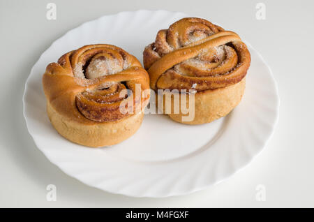 Two yeast sweet cinnamon rolls buns on white plate isolated on white table. Stock Photo