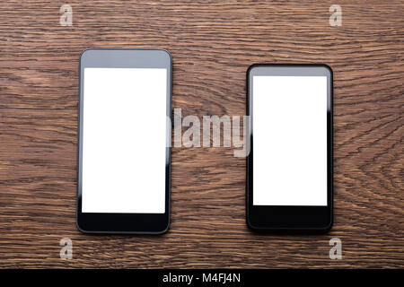 High Angle View Of Two Mobile Phones Showing Blank Screen On Wooden Desk Stock Photo