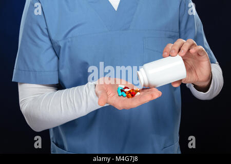 Cropped image of a smling male doctor dressed in uniform getting pills from a bottle isolated over dark background Stock Photo