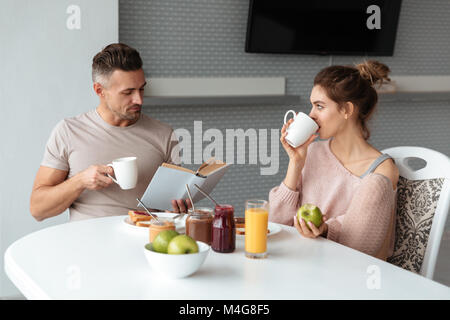 Portrait of a young loving couple having breakfast while sitting at the table in a kitchen at home and drinking coffee Stock Photo