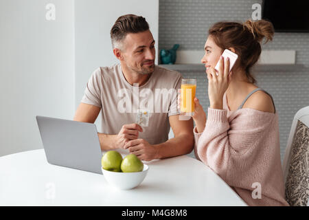 Portrait of a happy young couple shopping online with laptop computer while sitting at the table in a kitchen at home, man holding credit card and wom Stock Photo