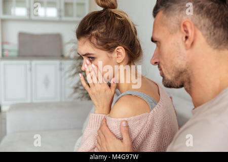 Back view of Careful man sitting on couch and calm down his upset girlfriend which crying at home Stock Photo