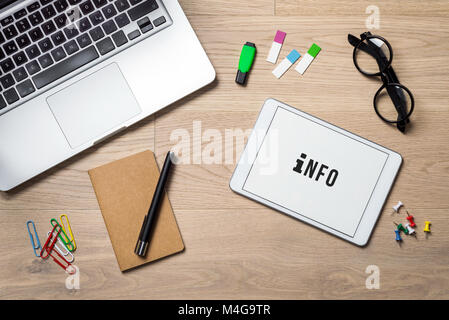 Info writing on tablet screen with laptop, notebook and glasses lying on wooden office desk as flat lay Stock Photo