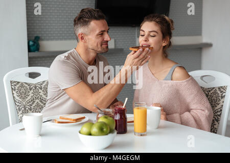 Portrait of a young loving couple having breakfast while sitting at the table in a kitchen at home Stock Photo