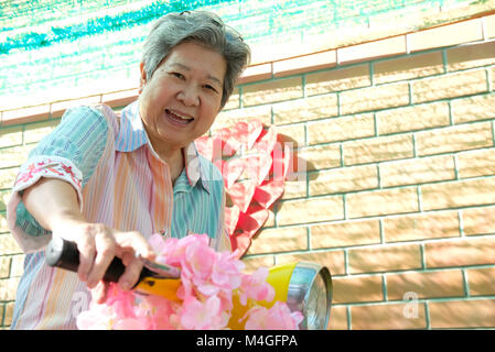 asian elder woman riding motorcycle. happy elderly female on yellow motorbike. fun mature lifestyle concept Stock Photo