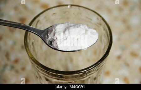 Dessert spoon with baking soda over the glass. Stock Photo