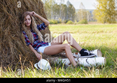 Young blonde country girl near haystacks on birh log Stock Photo