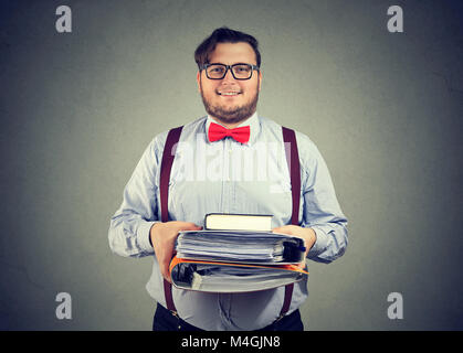 Smart man in eyeglasses holding pile of books and papers looking contently at camera. Stock Photo