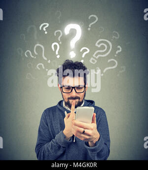 Young man having questions while using contemporary device in puzzlement. Stock Photo