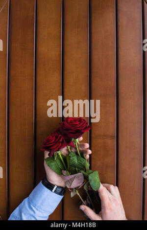 cropped image of man holding bouquet of red roses at table Stock Photo