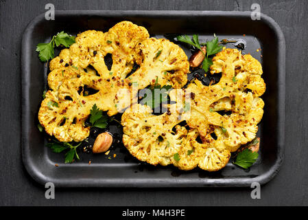 Roasted cauliflower steaks with greens and spices on baking sheet. Vegetarian vegan food. Top view, flat lay Stock Photo
