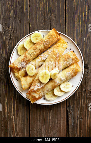 Thin pancakes, crepes roll with banana slices on wooden background with copy space. Top view, flat lay Stock Photo