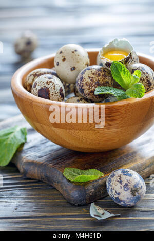 Whole and broken quail eggs in a wooden bowl. Stock Photo