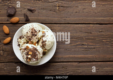 Tasty chocolate ice cream with nuts in bowl on wooden background with copy space. Top view, flat lay Stock Photo