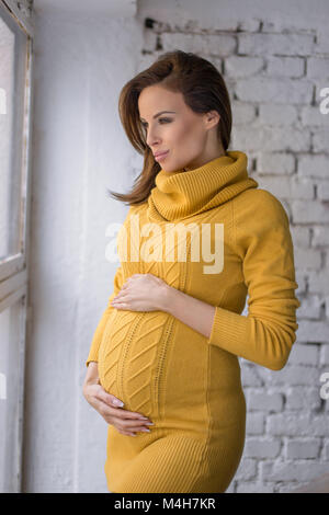 Pregnancy, motherhood, expectation concept - happy pregnant woman with big belly at window looking outside Stock Photo