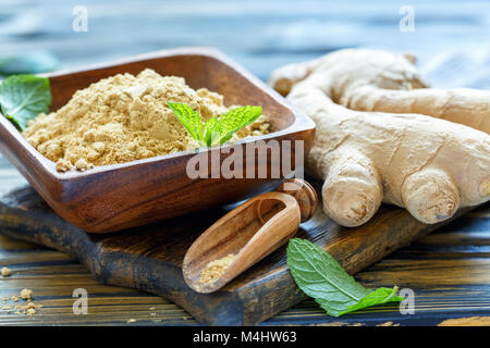 Ground ginger in a wooden bowl and ginger root. Stock Photo