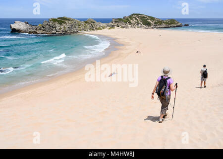 A female hiker walking with a hat, a bag and hiking pole on the beach of Robberg near Plettenberg Bay in South Africa with the beach and the Indian Oc Stock Photo