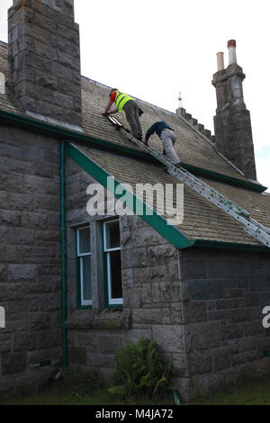 Two men looking to repair a leak on a roof Stock Photo