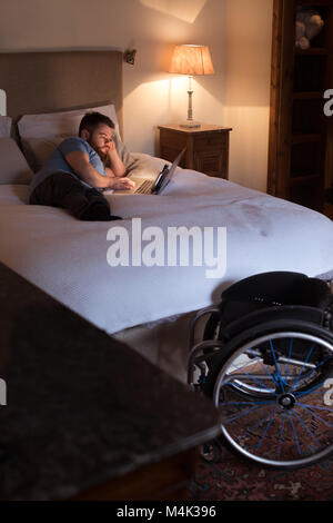 Disabled man using laptop in bedroom Stock Photo