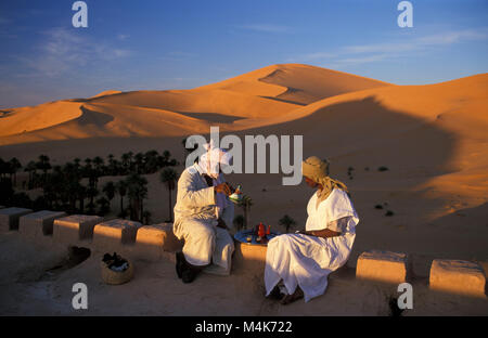 Algeria. Taghit or Tarit. Western Sand Sea. Grand Erg Occidental. Sahara desert. Sand dunes. Sand sea. Oasis. Men having tea, palm trees. Stock Photo