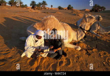 Algeria. Taghit or Tarit. Western Sand Sea. Grand Erg Occidental. Sahara desert. Bedouin, nomad with tourist looking at map with camel. Stock Photo