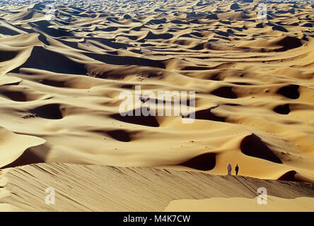 Algeria. Taghit or Tarit. Western Sand Sea. Grand Erg Occidental. Sahara desert. Sand dunes. Sand sea. Tourist, woman and bedouin walking, hiking. Stock Photo