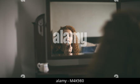 Woman applying lipstick in front of mirror Stock Photo