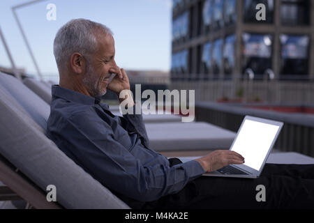 Businessman talking on mobile phone while working on laptop Stock Photo