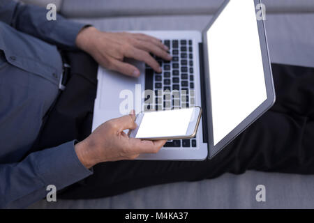 Businessman using mobile phone while working on laptop Stock Photo