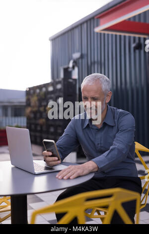 Businessman using mobile phone while working on laptop Stock Photo